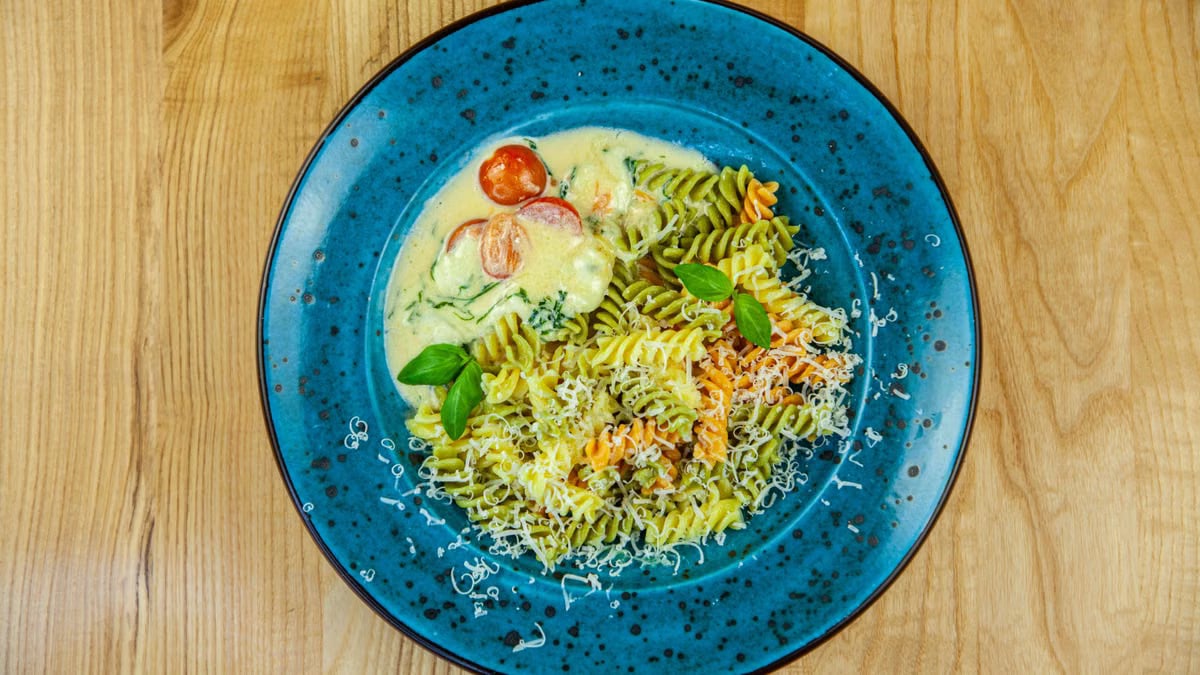 Colorful rotini pasta with cheese and tomatoes on a vibrant blue plate.